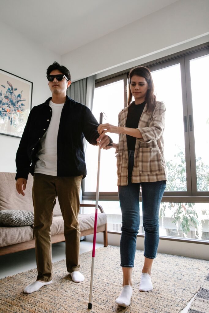 pexelsphoto71887277188727 Crystal Clear Eye Clinic Best Eye Clinic in Andheri Mumbai Man wearing sunglasses and a black jacket stands beside a woman who is guiding him with a white mobility cane in a bright living room